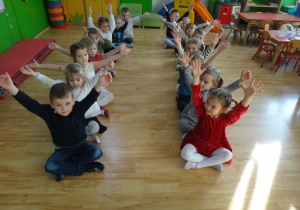 Dzieci siedzą na podłodze unosząc ręce w górę